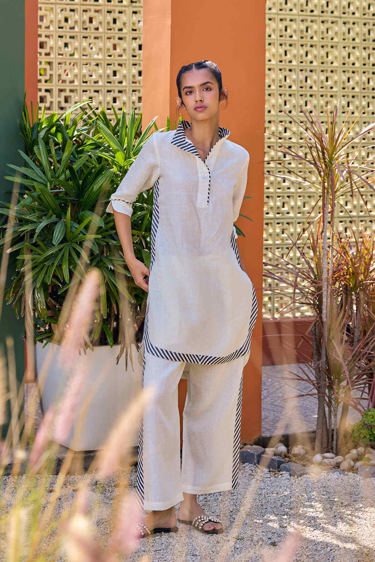 A woman wearing a beige linen kurti with striped detailing and matching wide-leg pyjamas standing outdoors